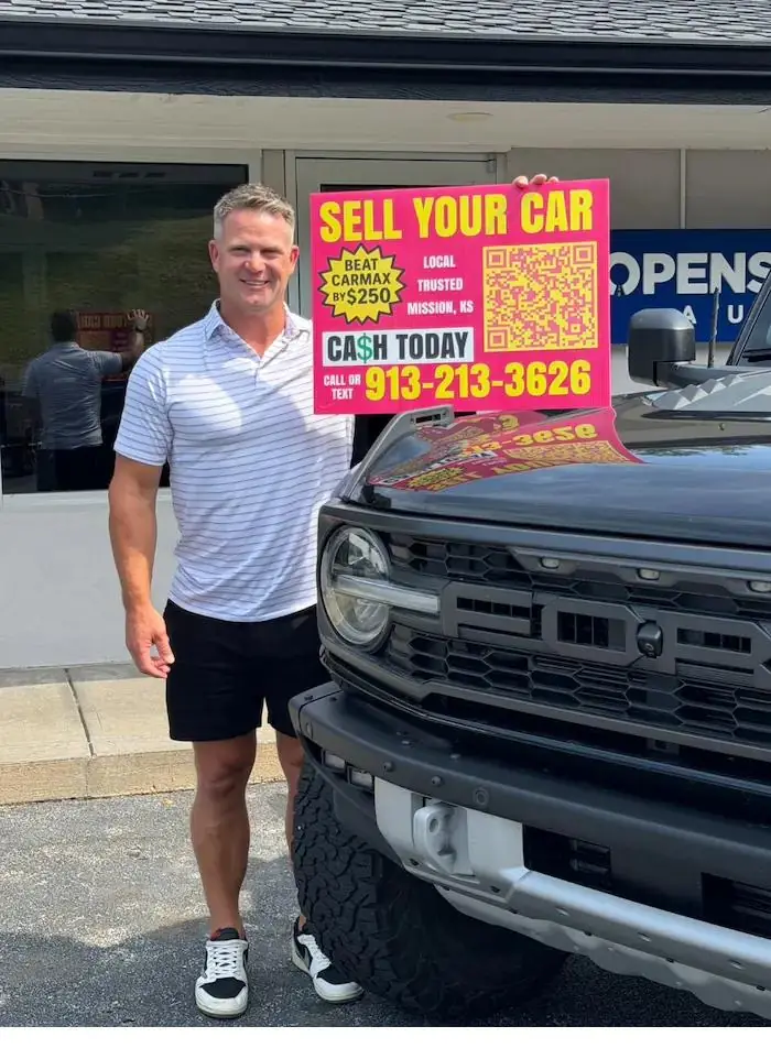 Kurt Breuckmann, founder of CarOfferly, outside the shop in Mission, Kansas holding a Sell Your Car sign